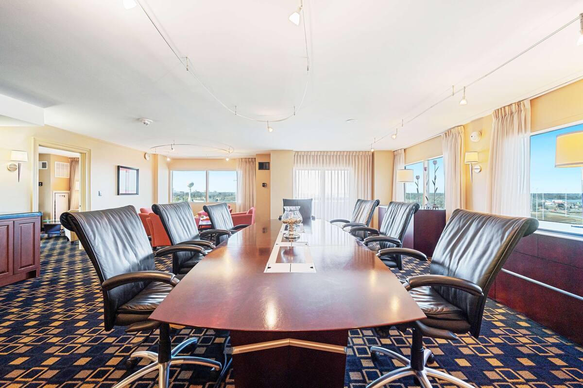 A conference room with a long table, multiple chairs, and a carpeted floor.