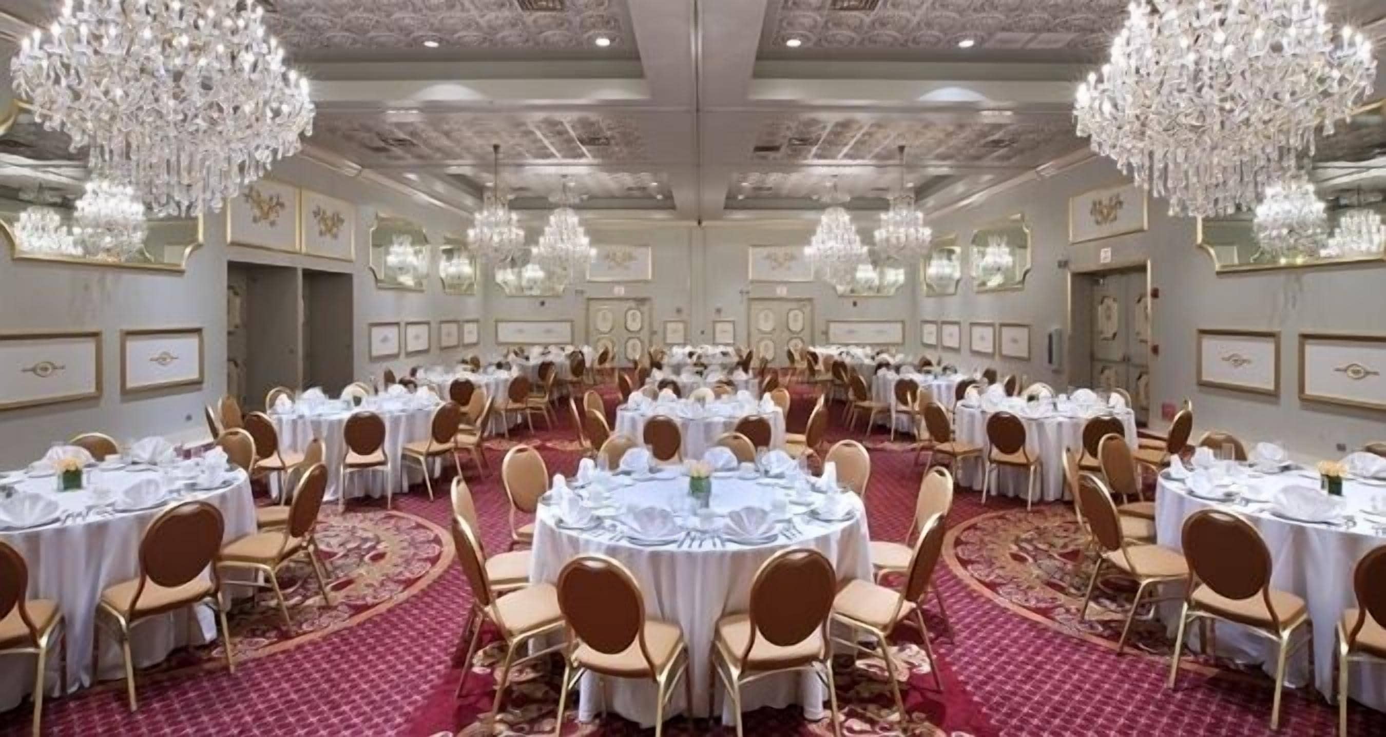 A banquet hall with round tables, chairs, chandeliers, and framed pictures on the walls.