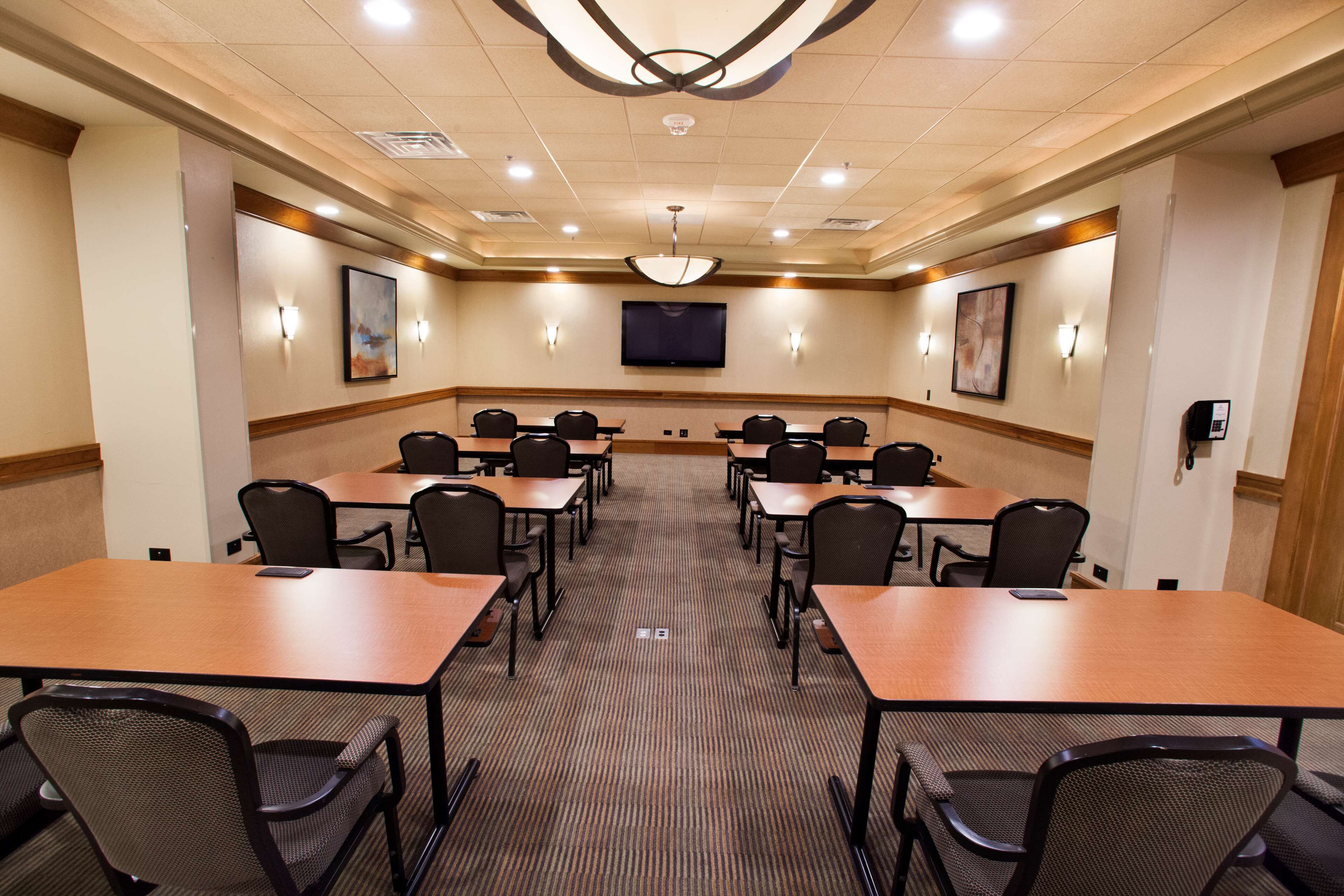 A conference room with multiple tables and chairs, a large screen, and wall-mounted lights.