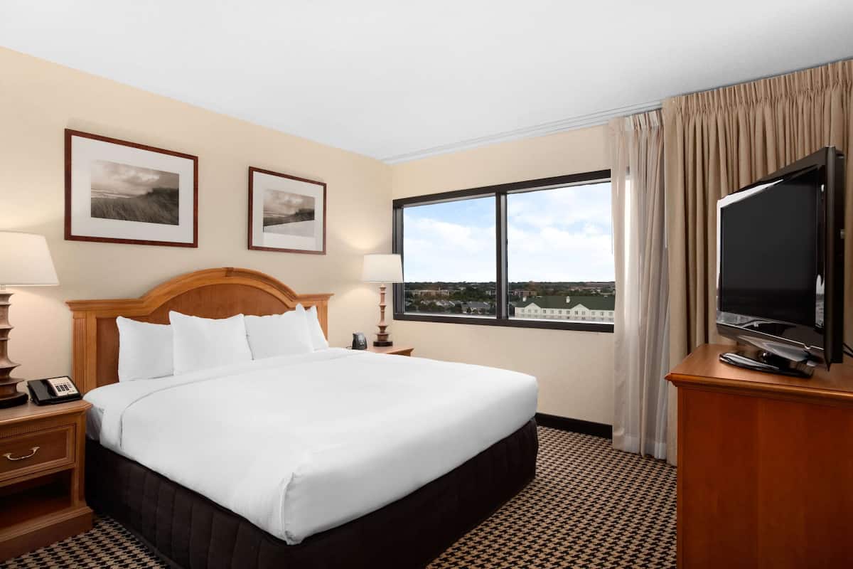 A hotel room with a large bed, a television on a wooden stand, a nightstand with a lamp, and two framed pictures on the wall.