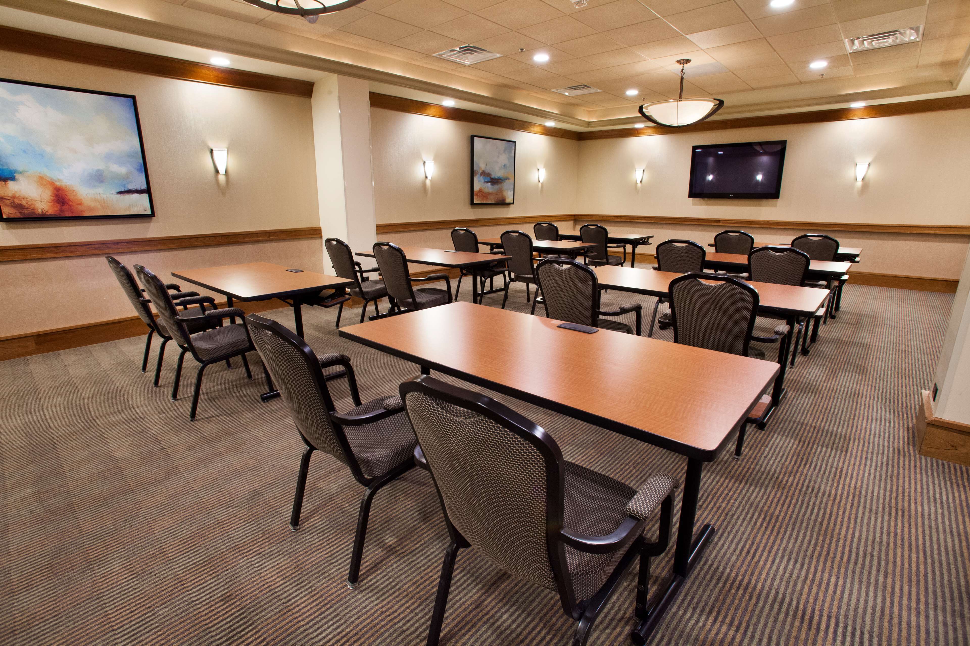 A conference room with multiple tables and chairs, a flat-screen TV, and artwork on the walls.