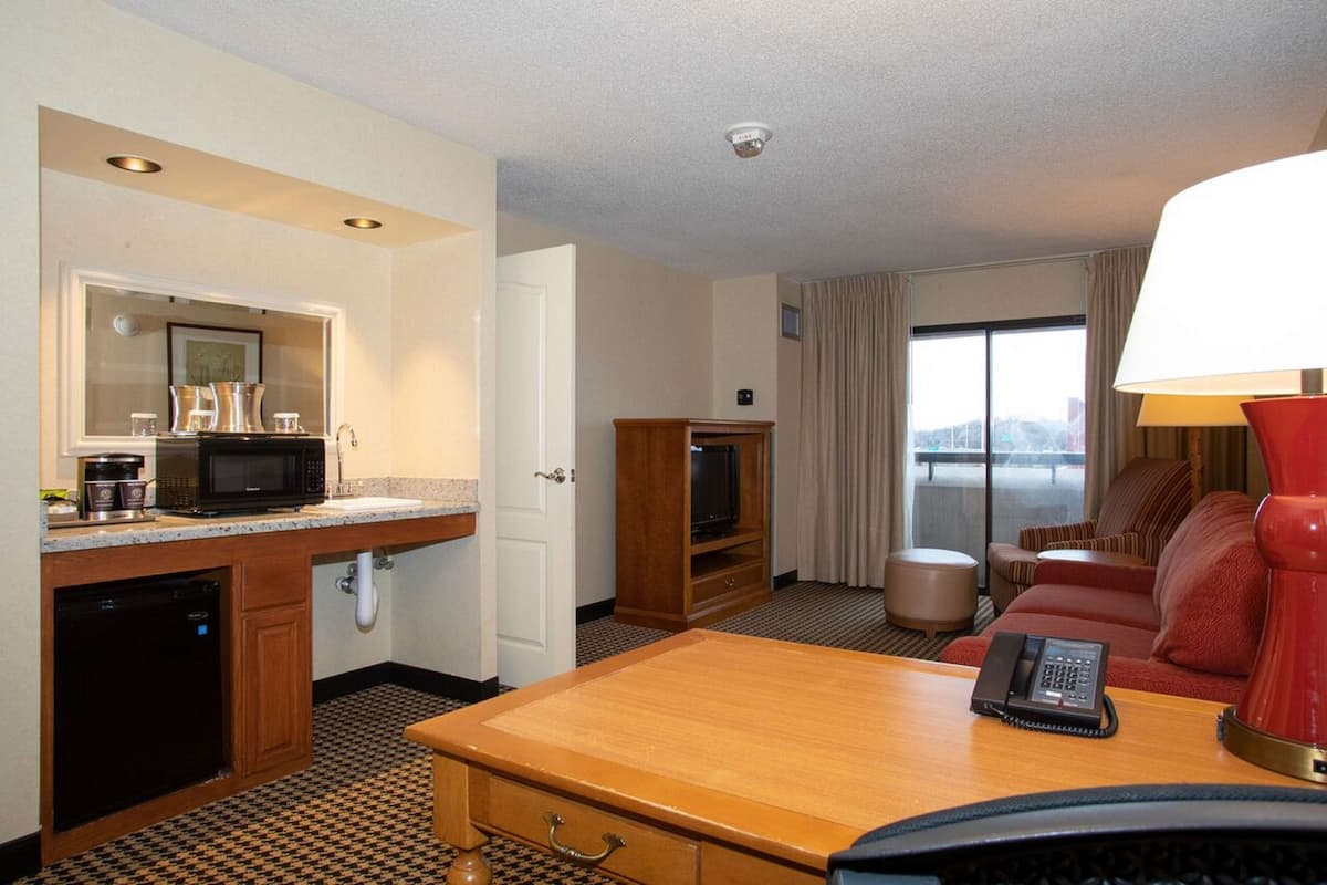 A hotel room with a kitchenette, a television, a sofa, and a desk with a telephone.