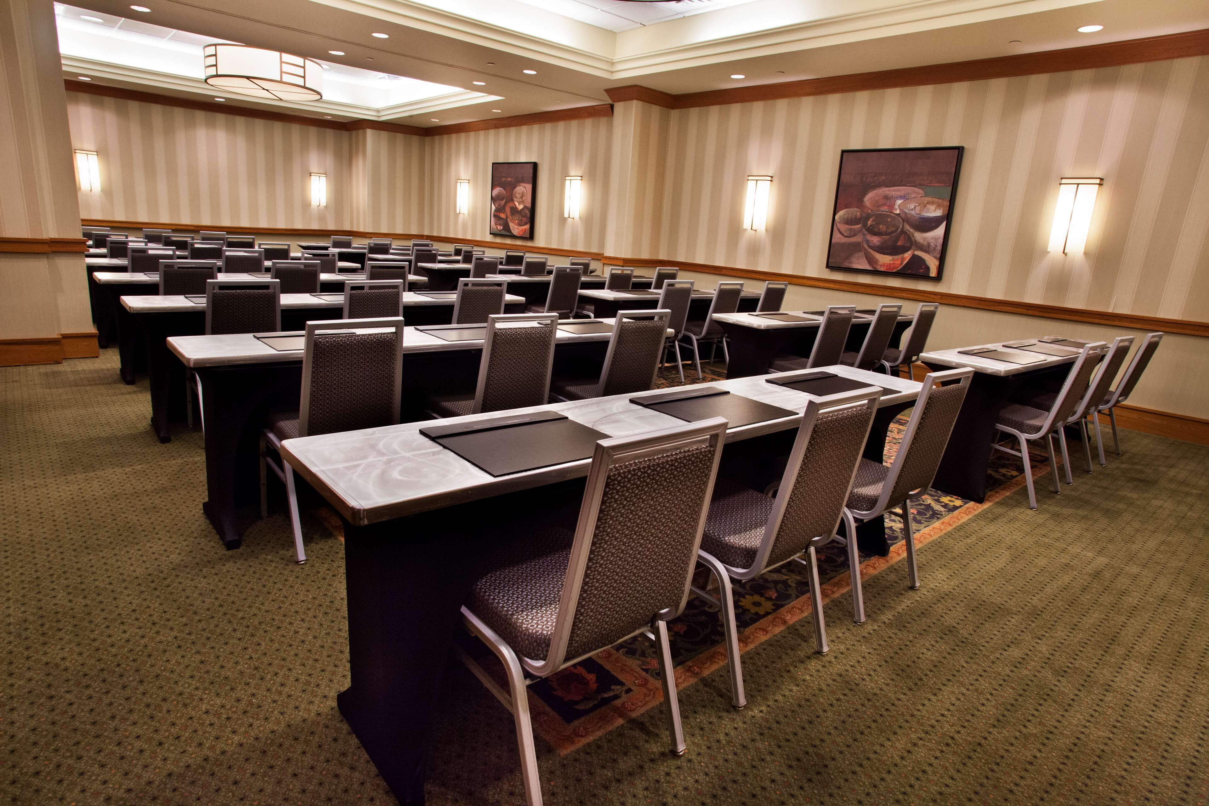 A conference room with rows of tables and chairs, carpeted flooring, and wall-mounted lighting.