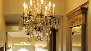 A hotel lobby with a chandelier, a mirror, and a red carpet leading to an elevator.