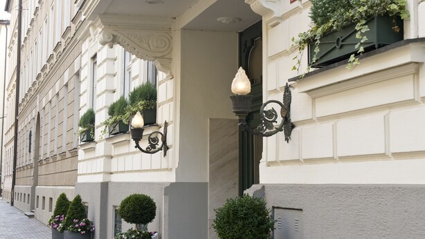 A hotel with a classic facade, a signboard, and potted plants.