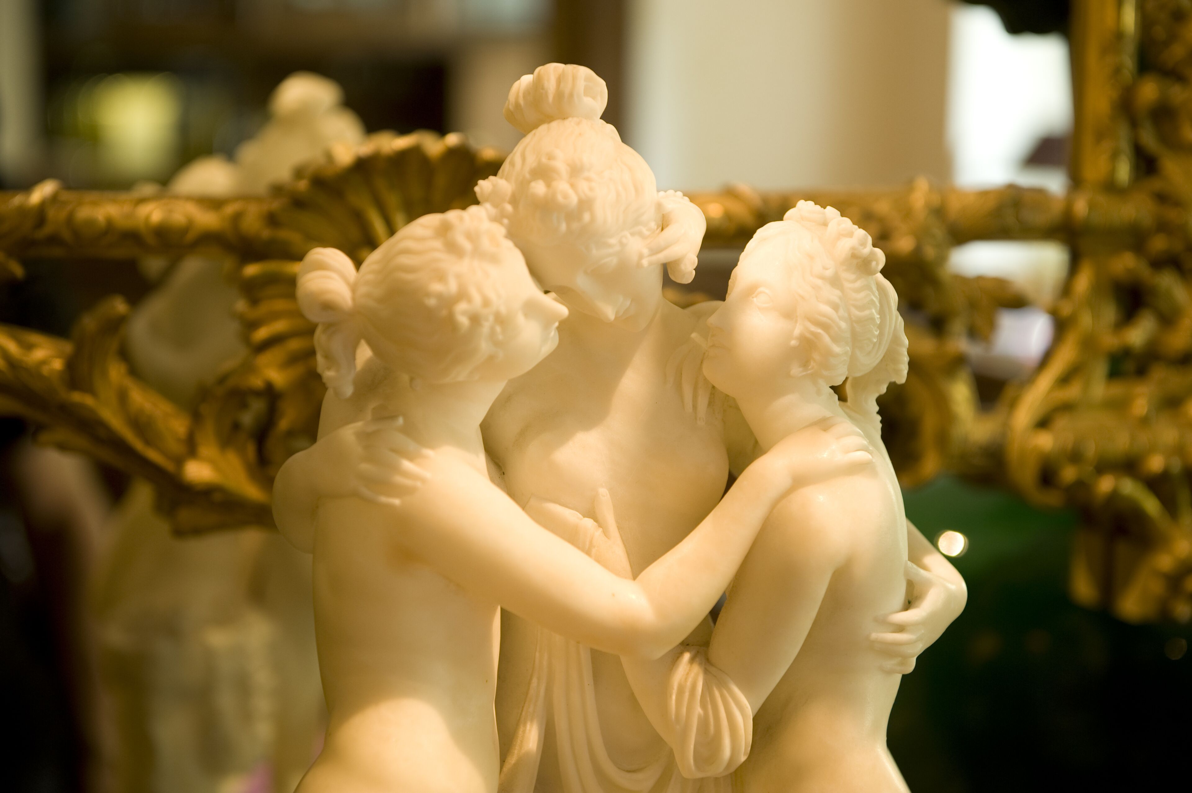 Close-up de uma escultura em mármore branco retratando três figuras a abraçar.