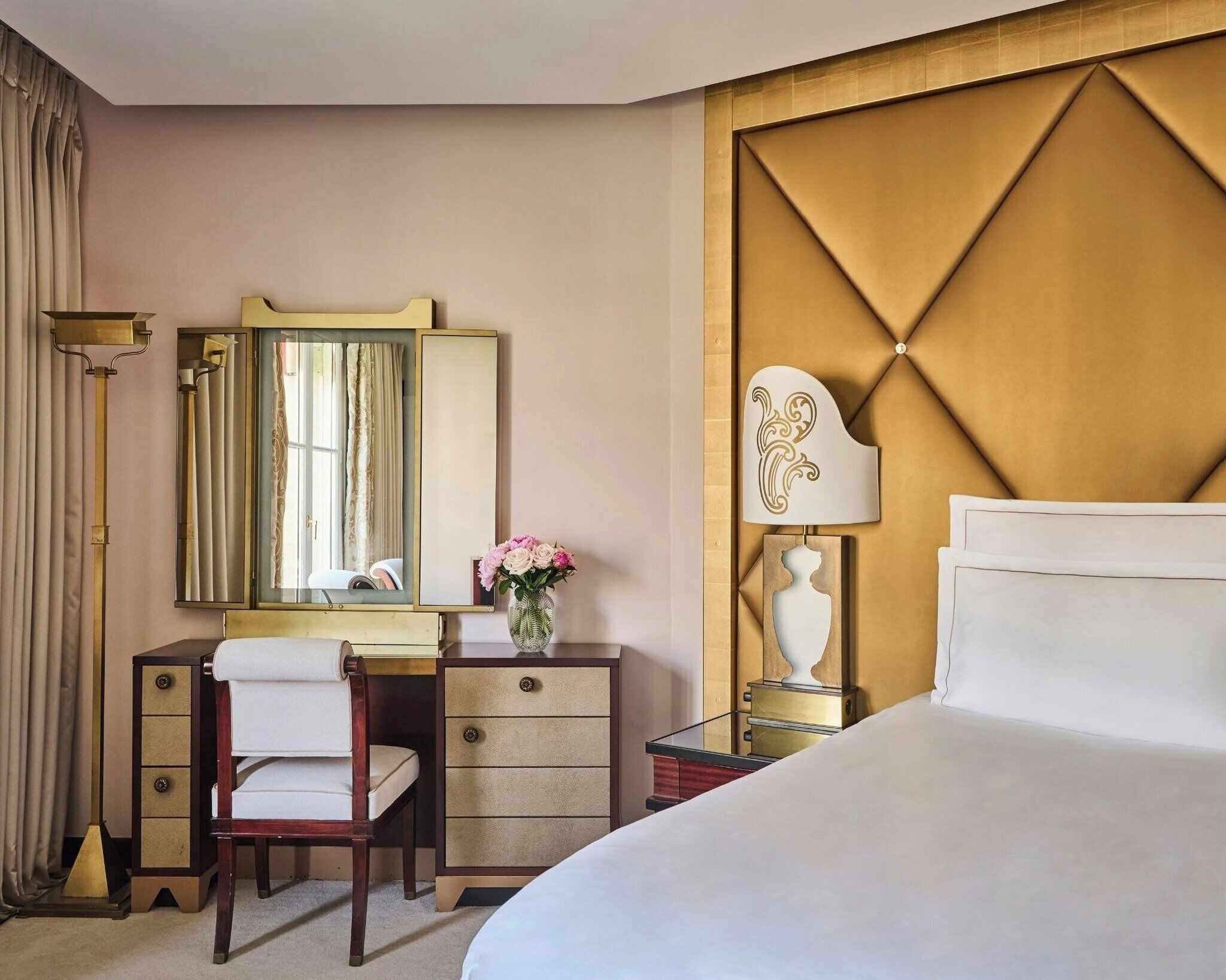 Ein Hotelzimmer mit einem Bett, einem Schreibtisch mit Stuhl, einem Schminktisch mit Spiegel und einem Nachttisch mit Lampe.