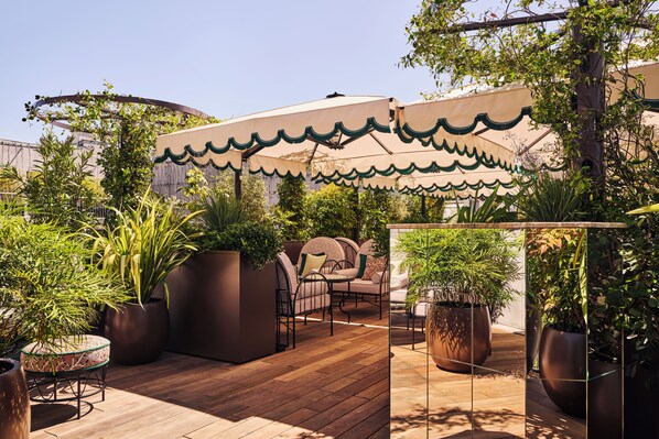 An outdoor patio with wooden flooring, potted plants, and a seating area with chairs and a table. - Hôtel Fouquet's Paris (Paris)