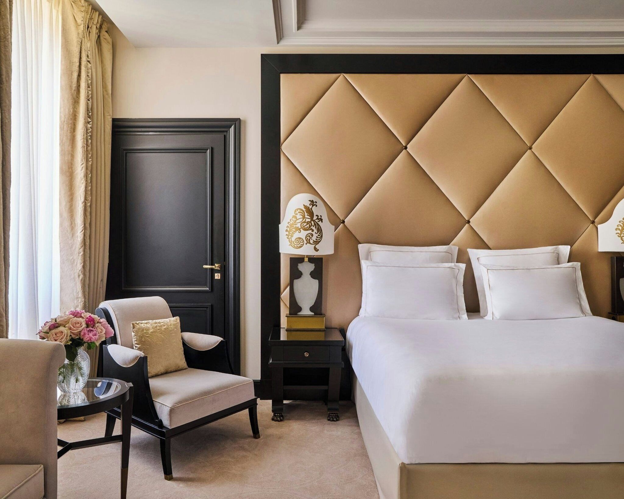 A hotel room with a large bed, a chair, a nightstand, a lamp, and a door.