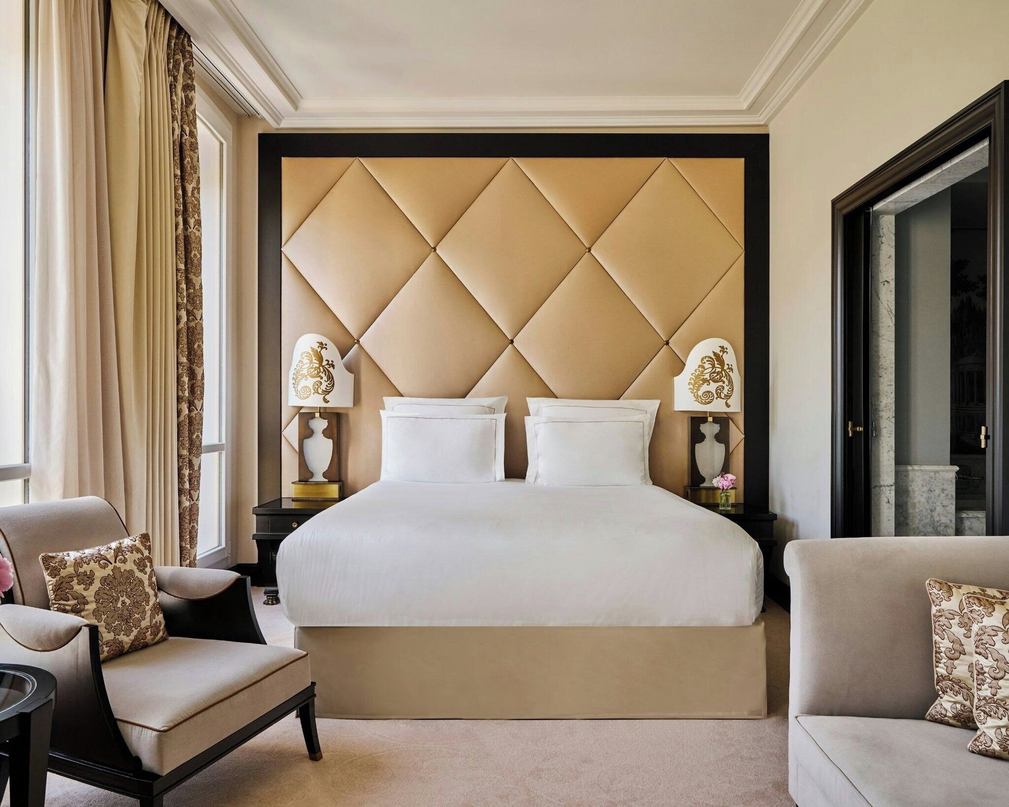 A hotel room with a large bed, two bedside tables with lamps, a chair, and a sofa.