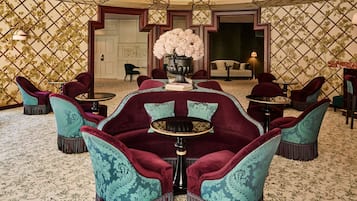 Una habitación con una zona de estar central que incluye un sofá y sillones, un jarrón decorativo con flores, y una pared con estampado.