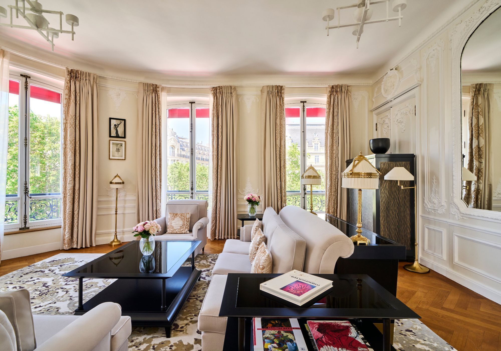 A room with a sofa, a coffee table, a fireplace, and large windows with curtains.