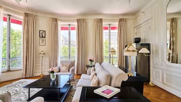 A room with a sofa, a coffee table, a fireplace, and large windows with curtains.