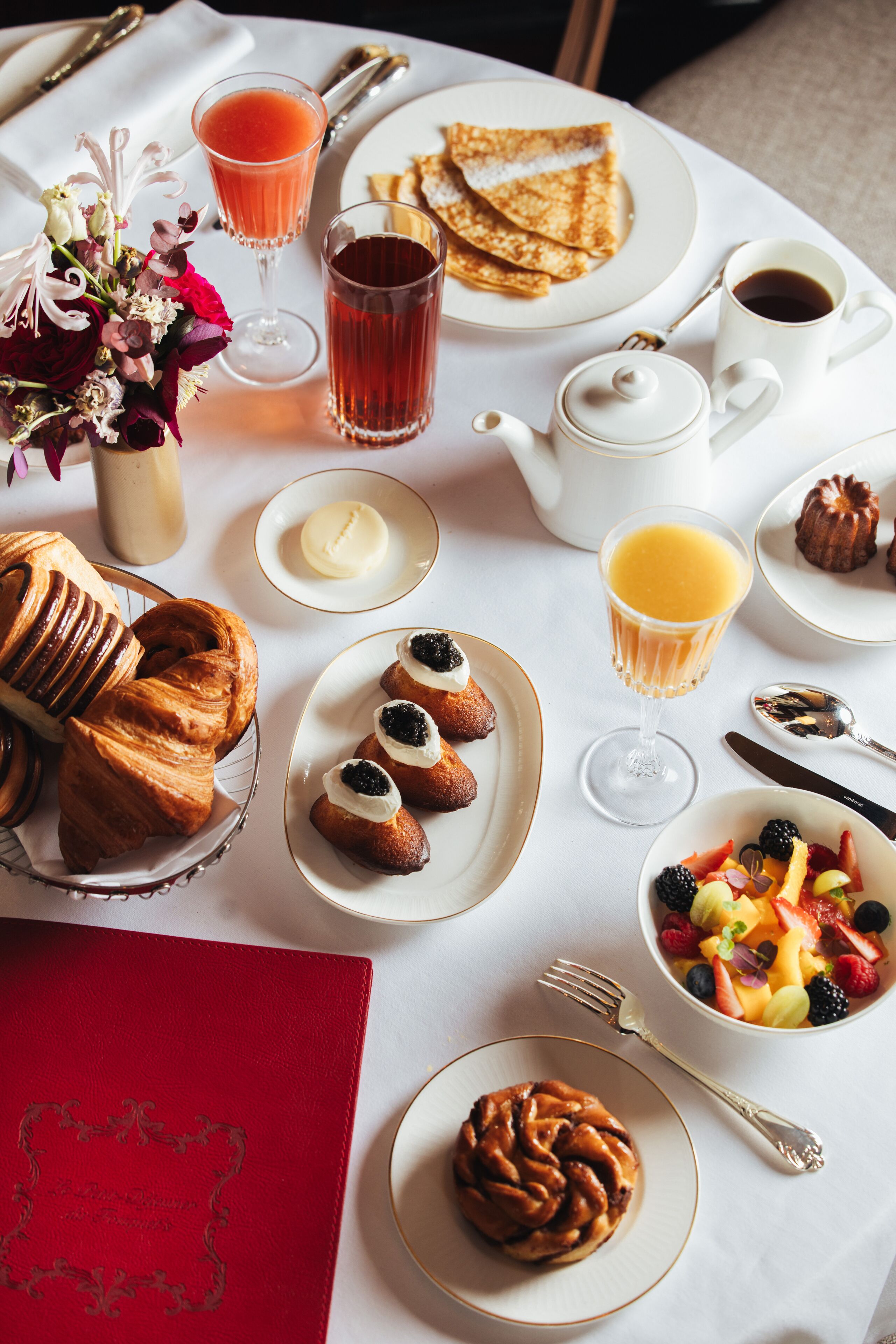 A breakfast table with croissants, pastries, fruit, coffee, and juice.