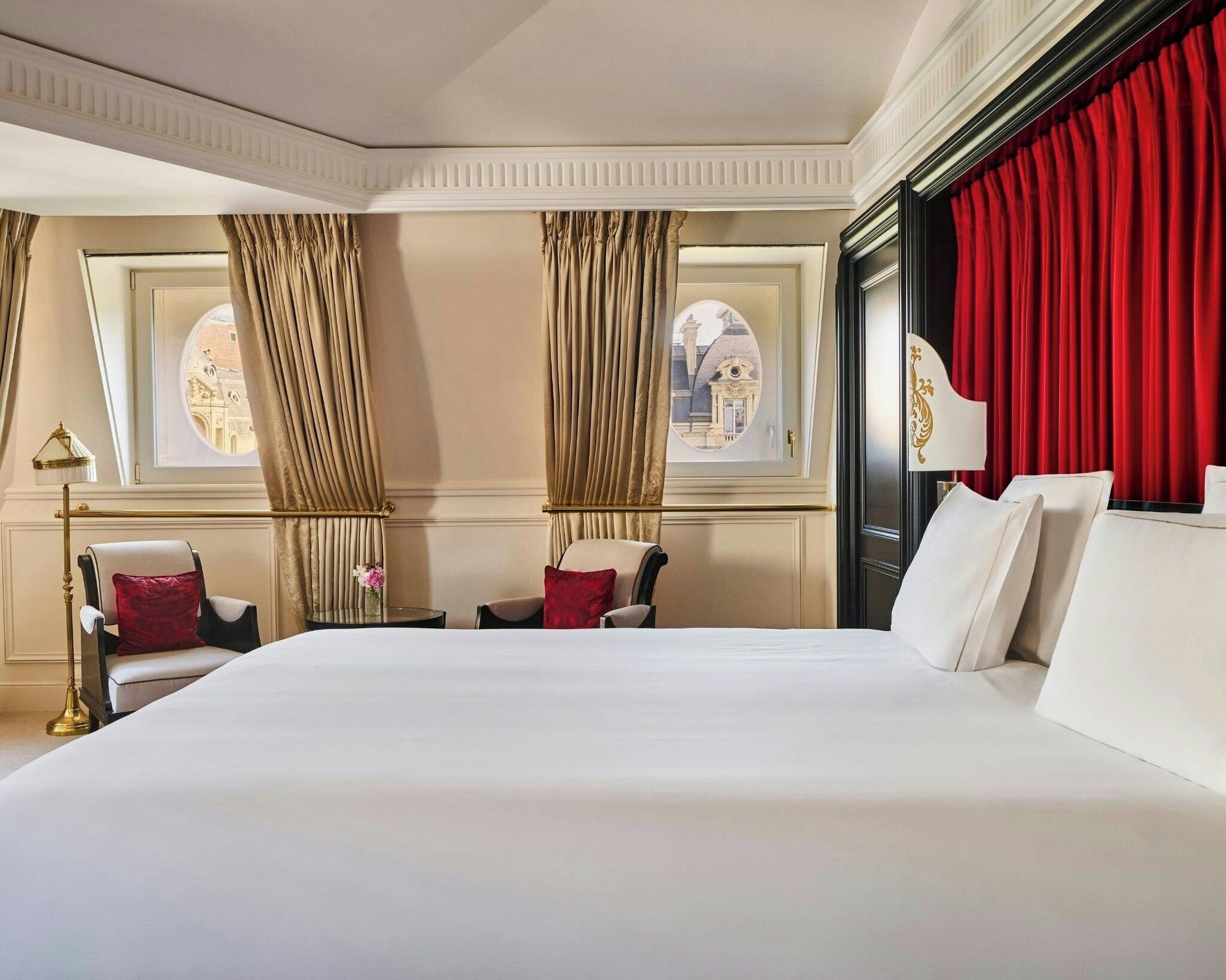 Une chambre d’hôtel avec un grand lit, deux chaises, une table et une fenêtre avec des rideaux.