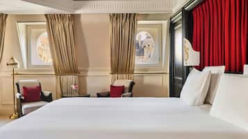 A hotel room with a large bed, two chairs, a table, and a window with curtains.