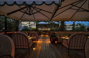 Una veranda esterna con mobili in vimini, un pontile in legno e vista su edifici sullo sfondo.
