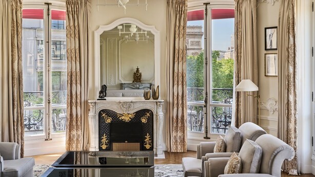 Una habitación lujosa con chimenea, muebles elegantes y ventanas amplias con cortinas.