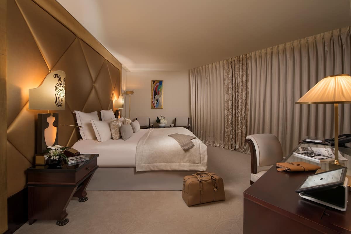A hotel room with a large bed, bedside tables, a desk with a laptop, and a chair.
