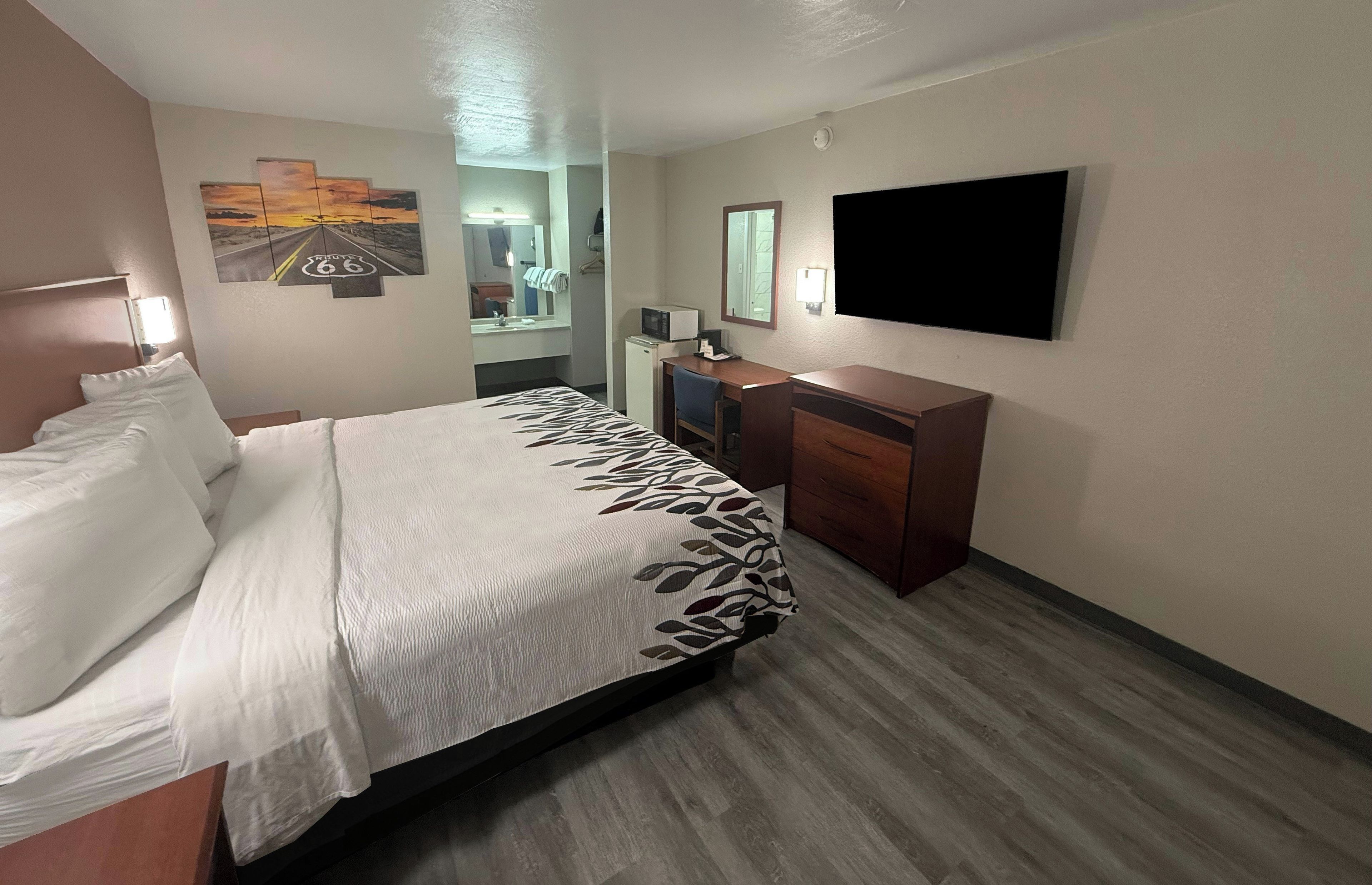 A hotel room with a bed, a desk, a flat-screen TV, and a painting on the wall.