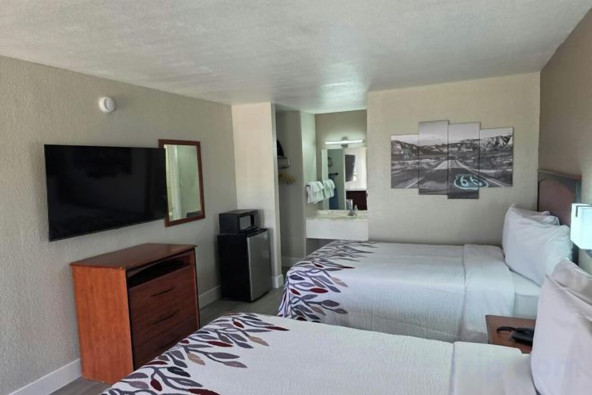 A hotel room with two beds, a TV, a desk with a computer, and a mirror.
