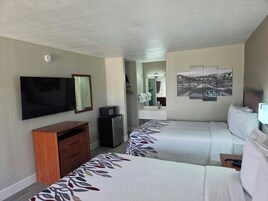 Habitación de hotel con dos camas, televisión, cómoda, espejo y una obra de arte colgada en la pared.