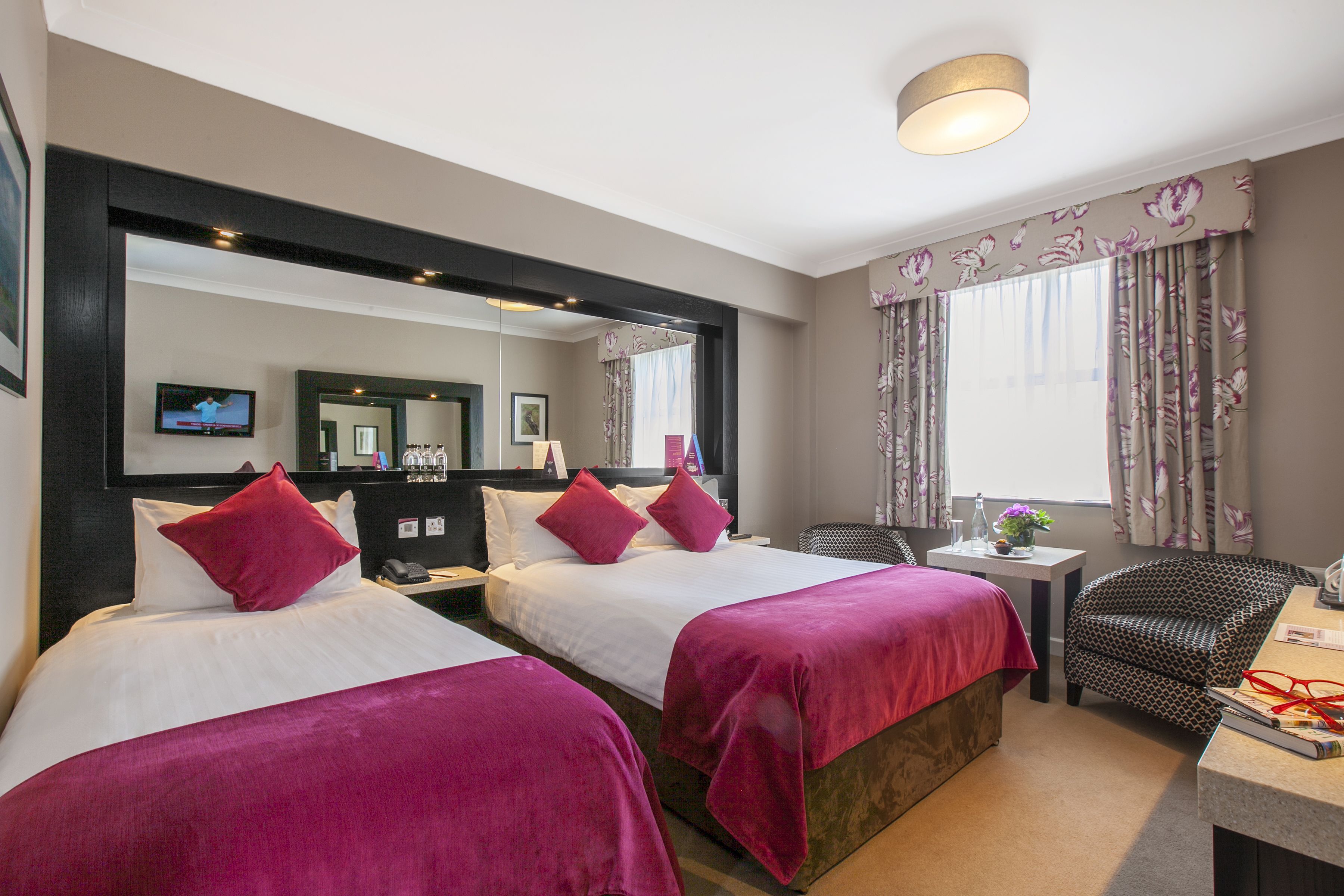 A hotel room with two beds, a desk, a chair, a TV, and a large mirror.