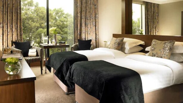 A hotel room with two beds, a desk, and a chair. There is a large window with curtains, and a mirror on the wall. - Ashling Hotel Dublin (Dublin)