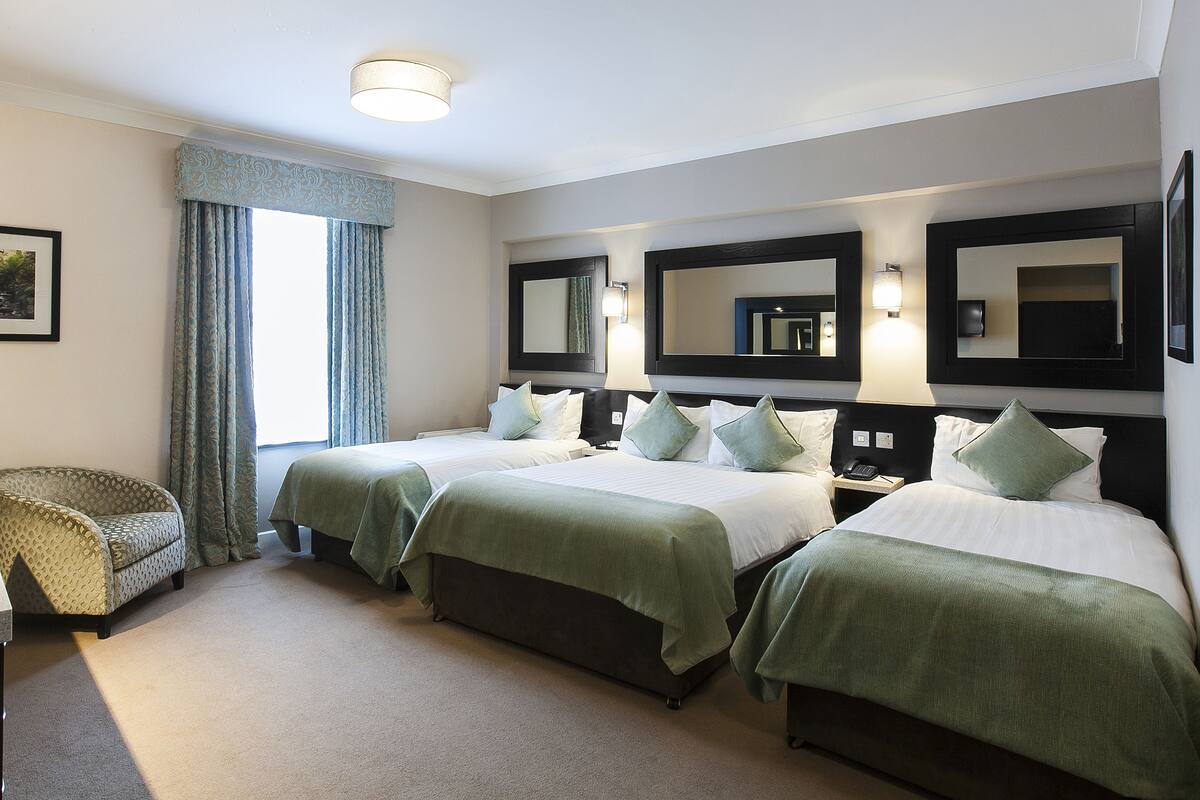 Habitación de hotel con dos camas, una silla y una mesita de noche.