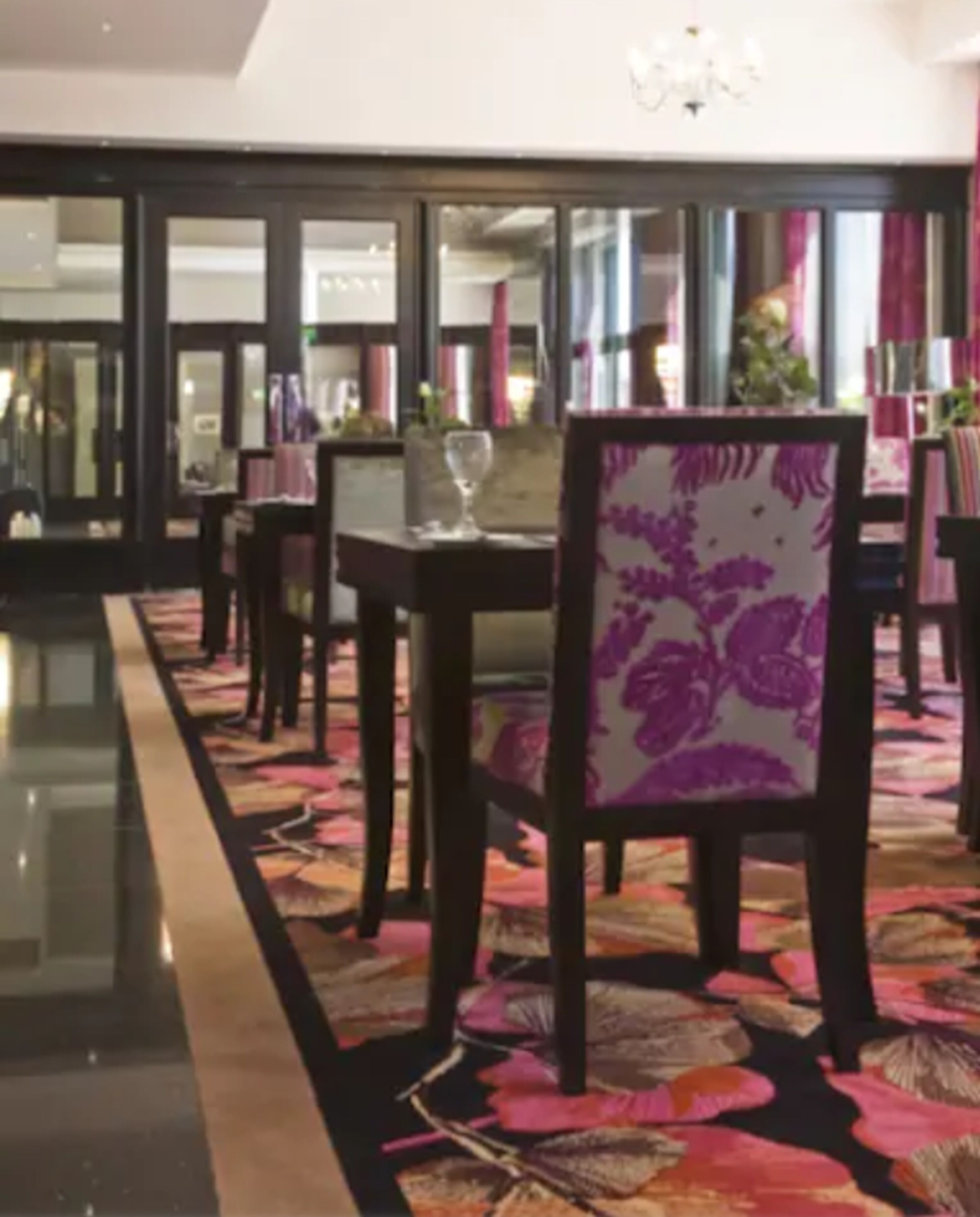 A hotel lobby with a long, polished corridor, a dining area with tables and chairs, and a chandelier.