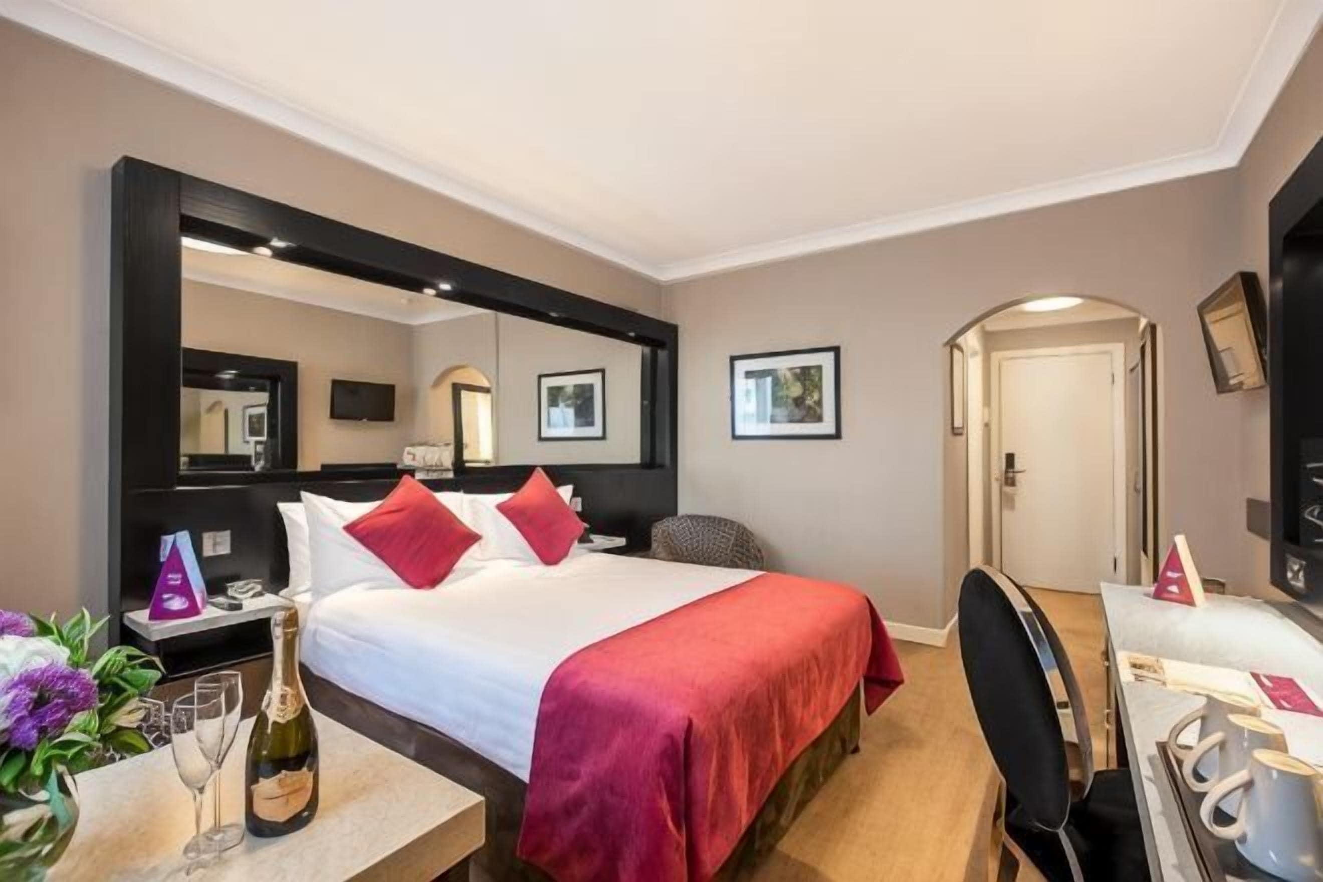 Habitación de hotel con cama, escritorio, silla, televisor y espejo.