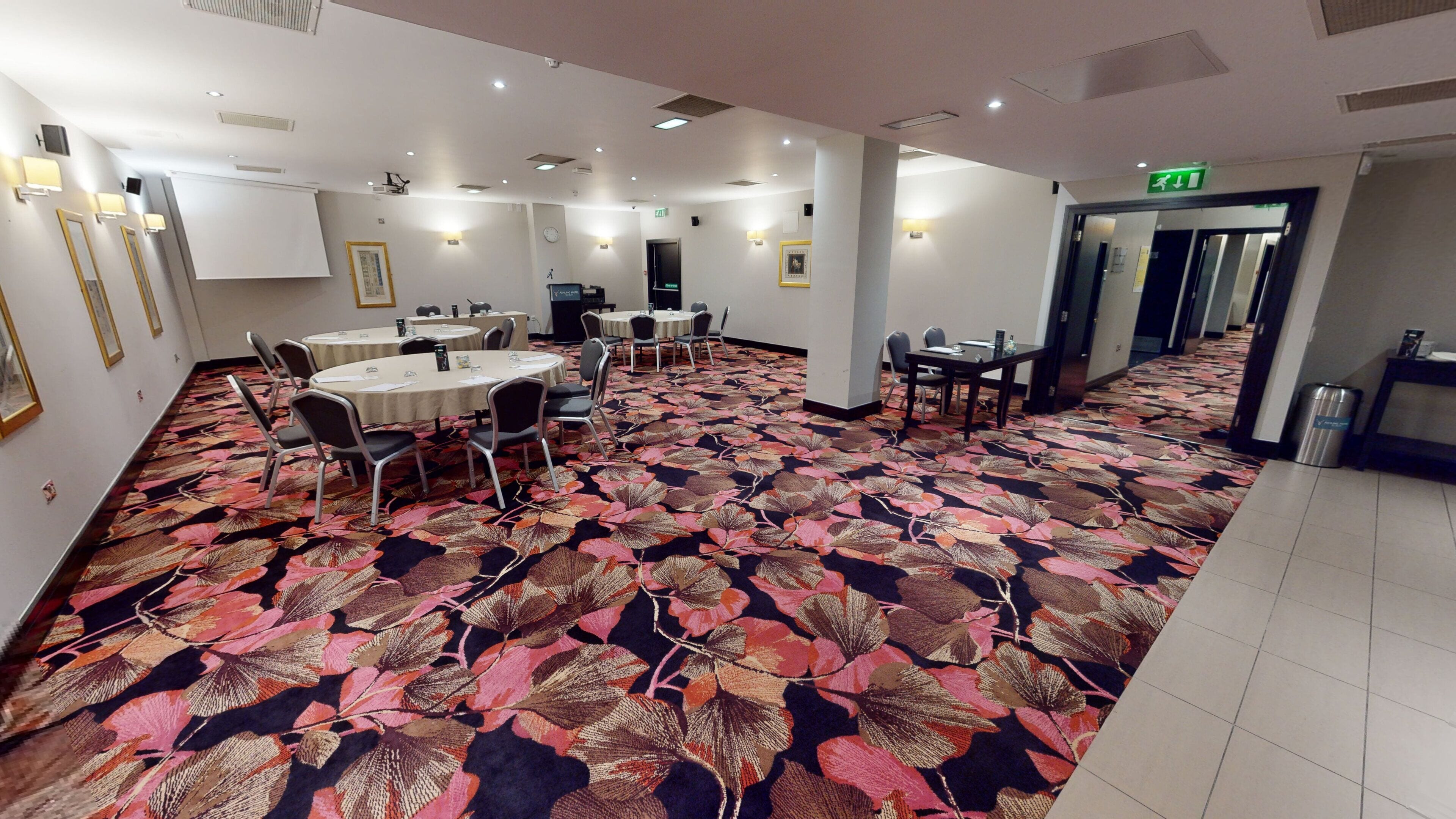 Une salle de conférence d’hôtel avec des tables rondes, des chaises et un tapis à motifs.