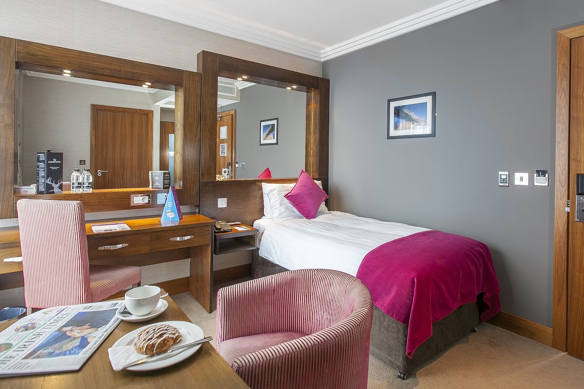 Habitación de hotel con cama, escritorio, silla, espejo y puerta.