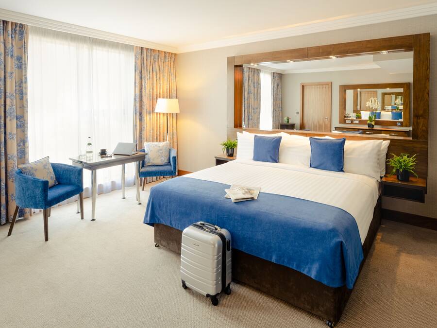 Una habitación de hotel con una cama grande, un escritorio con una computadora portátil, una silla y una maleta.