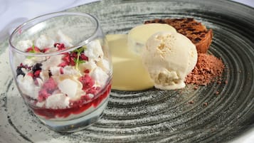 Un plato de postre con un vaso de compota de bayas y dos bolas de helado de vainilla.
