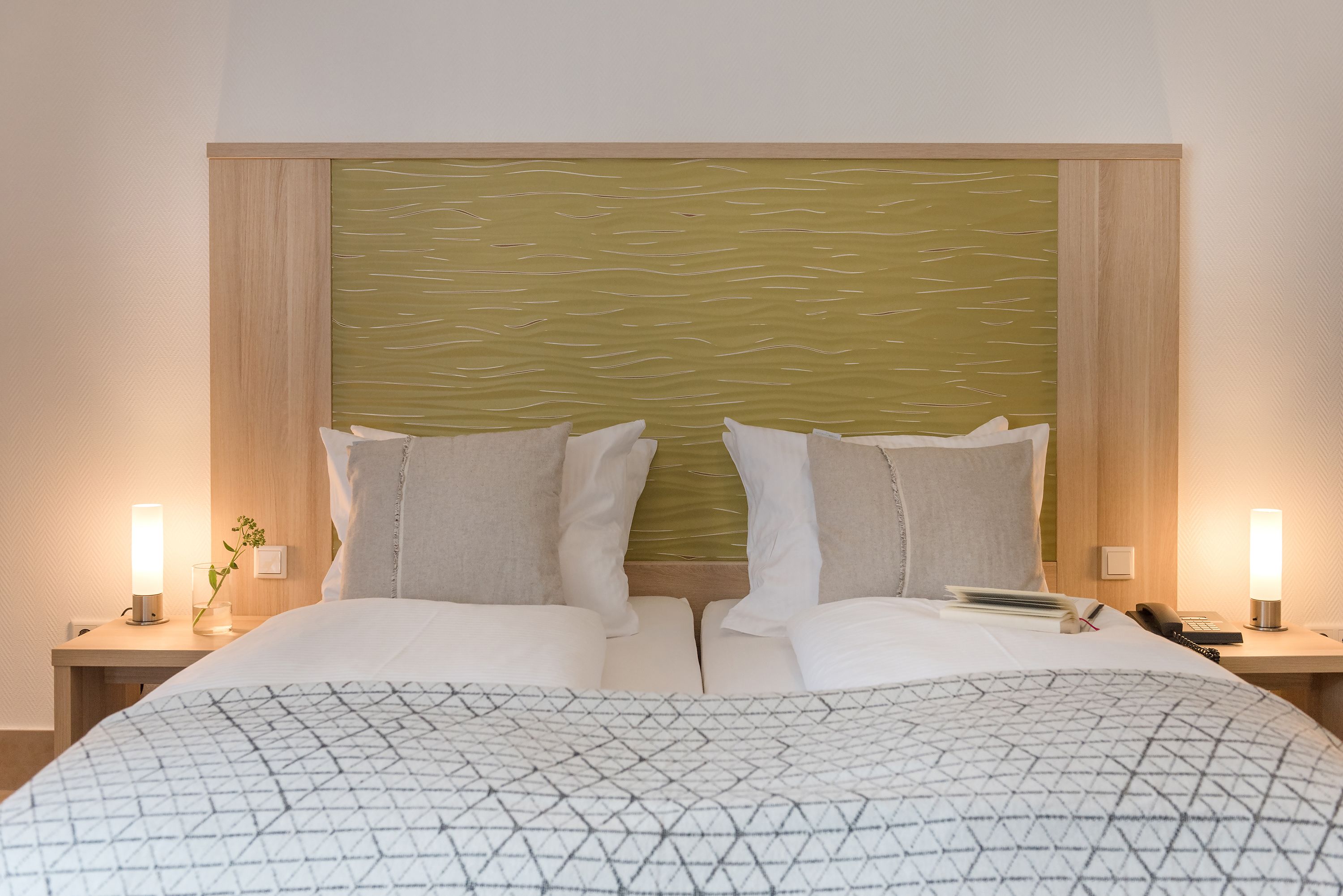 A hotel room with a large bed, two bedside tables, a nightstand, a lamp, and a wall-mounted panel.