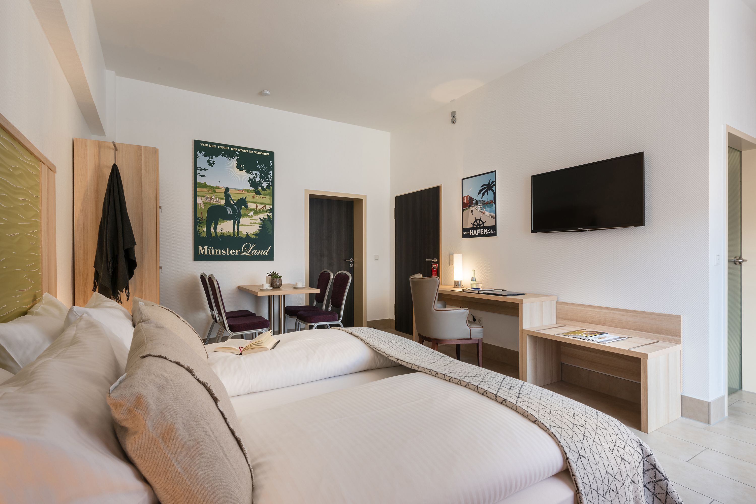 A hotel room with a bed, a desk, a chair, a TV, and a poster on the wall.
