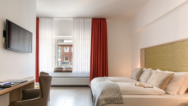 Une chambre d’hôtel moderne équipée d’un lit, d’un bureau, d’une chaise, d’une télévision et d’une fenêtre avec des rideaux.