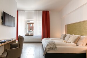 Una habitación de hotel moderna con una cama, un escritorio, una silla, un televisor y una ventana con cortinas.