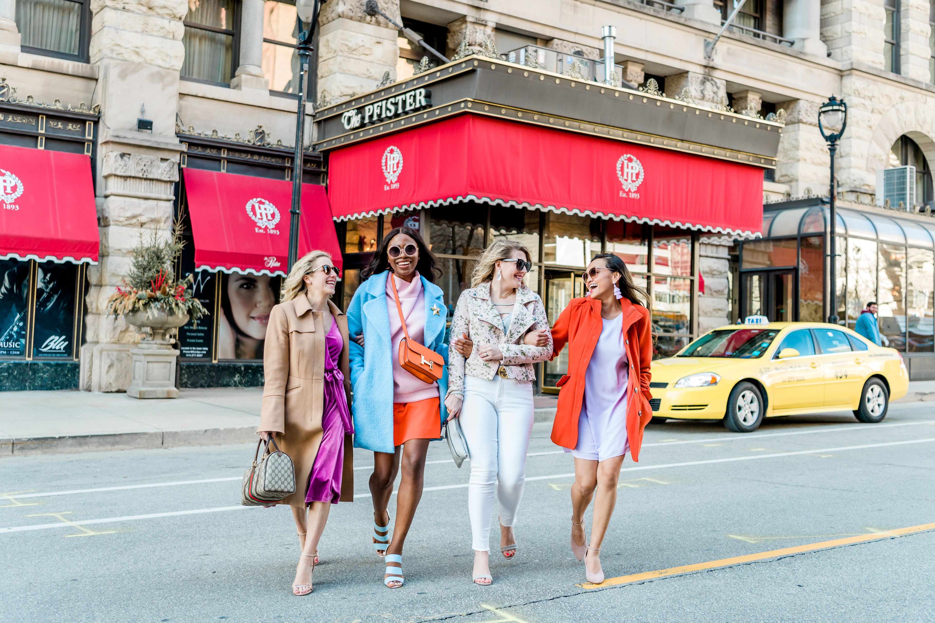 Un groupe de personnes marchant dans une rue, devant un immeuble orné d’une marquise rouge et d’une enseigne sur laquelle on peut lire « The Pfister ».