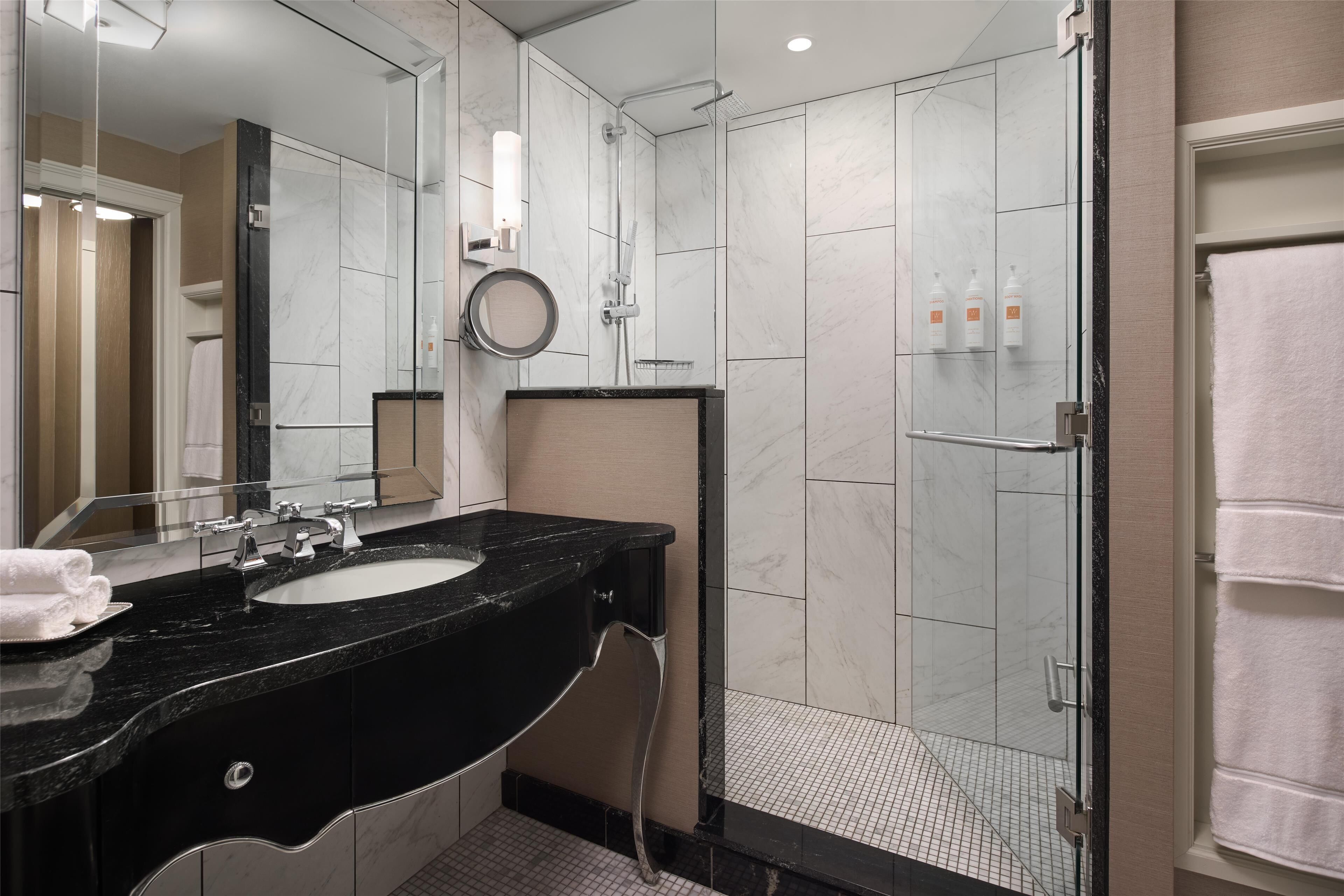 Un bagno moderno con un lavabo in marmo nero, uno specchio grande e una cabina doccia in vetro.