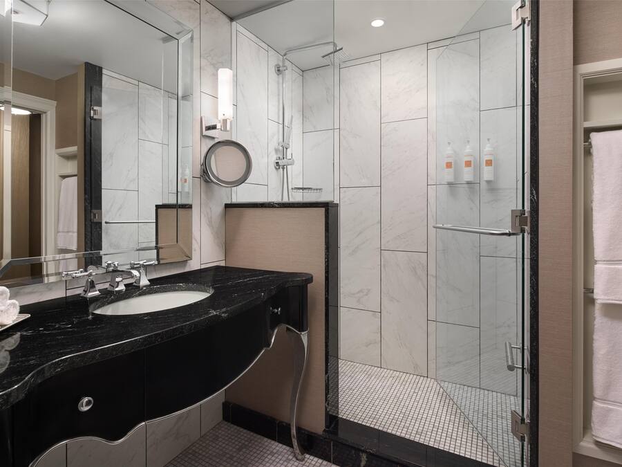 Une salle de bain moderne avec un lavabo en marbre noir, un grand miroir et une douche à parois de verre.