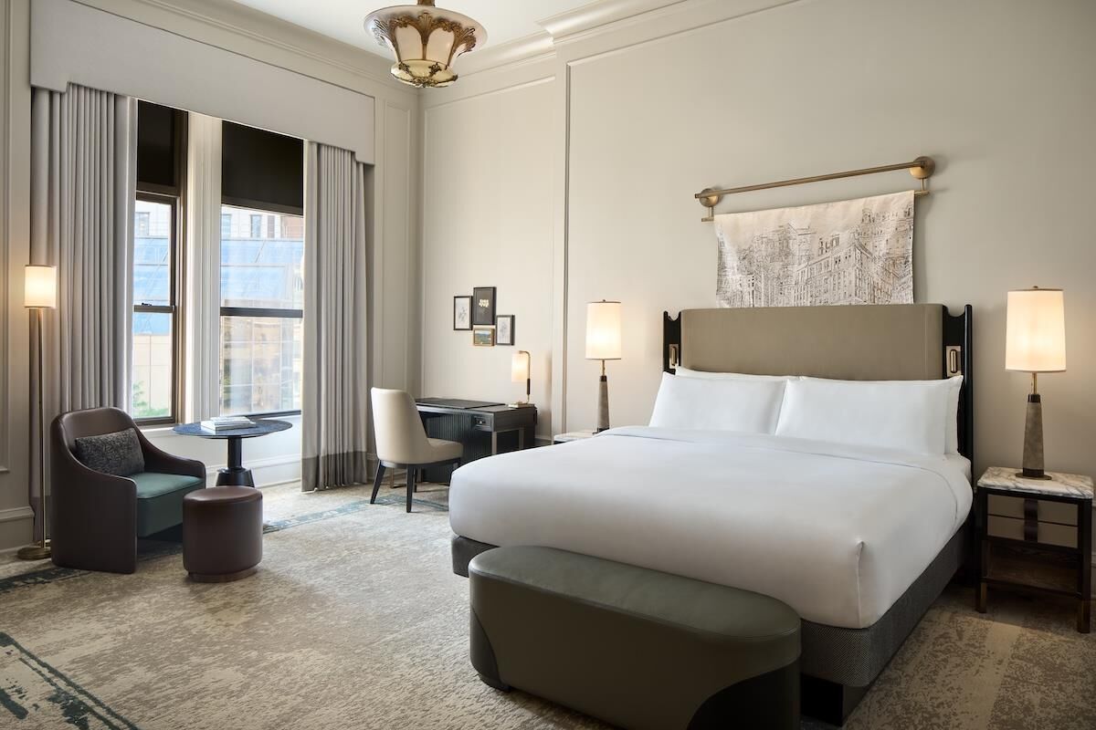 Une chambre d’hôtel avec un grand lit, un bureau, deux chaises, une petite table et une lampe.