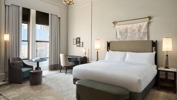 A hotel room with a large bed, a desk, two chairs, a small table, and a lamp.