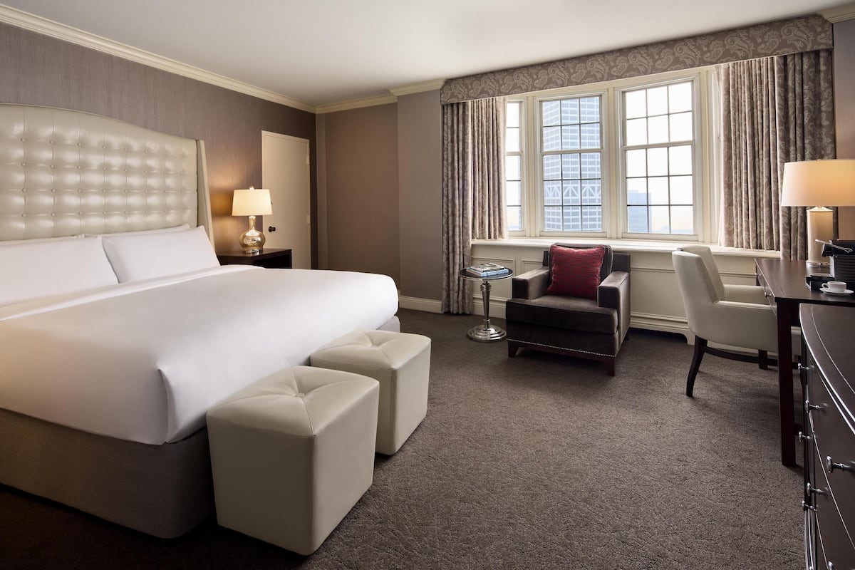 A hotel room with a large bed, a desk, a chair, and a small table.