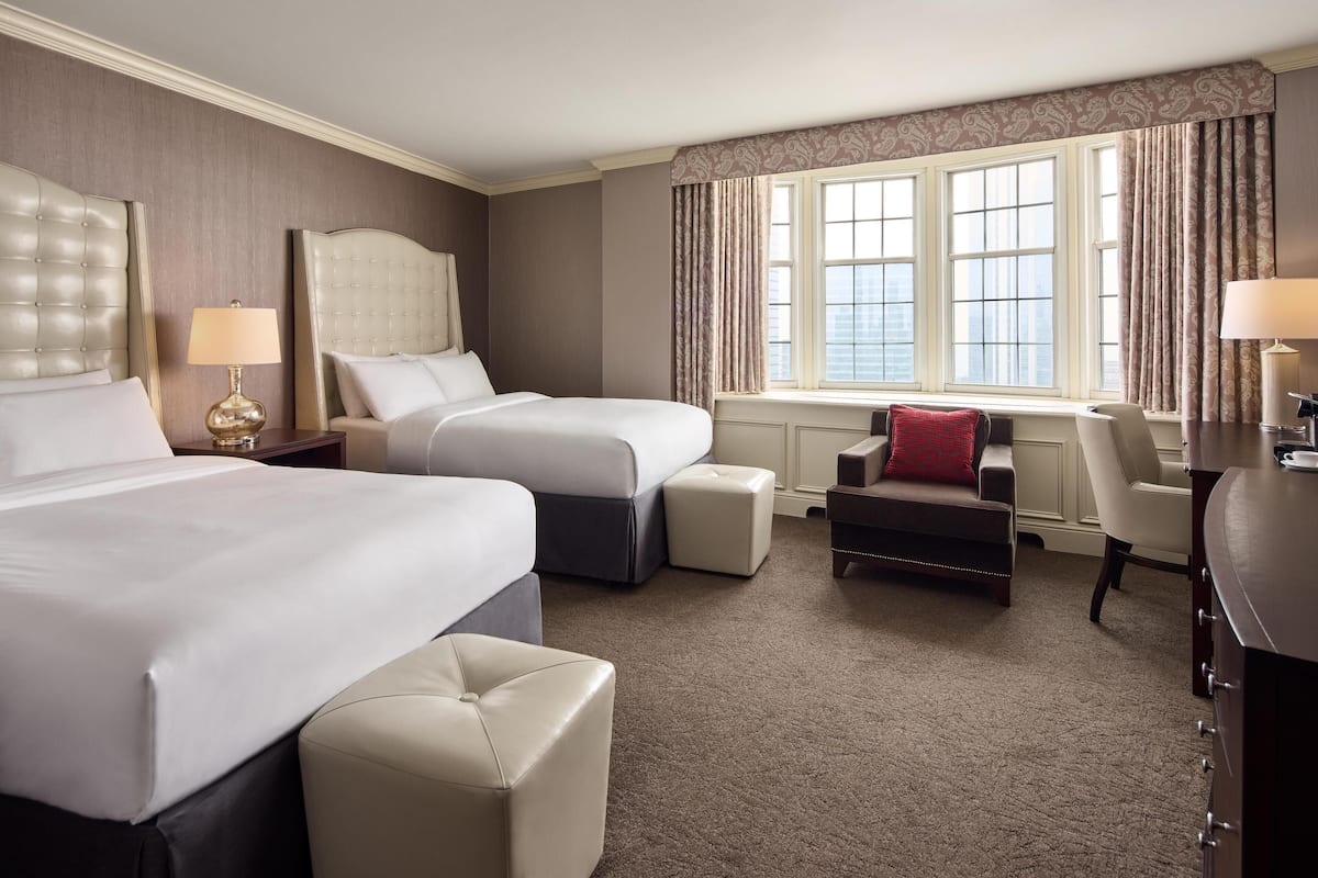 A hotel room with two beds, a desk, a chair, and a window with curtains.