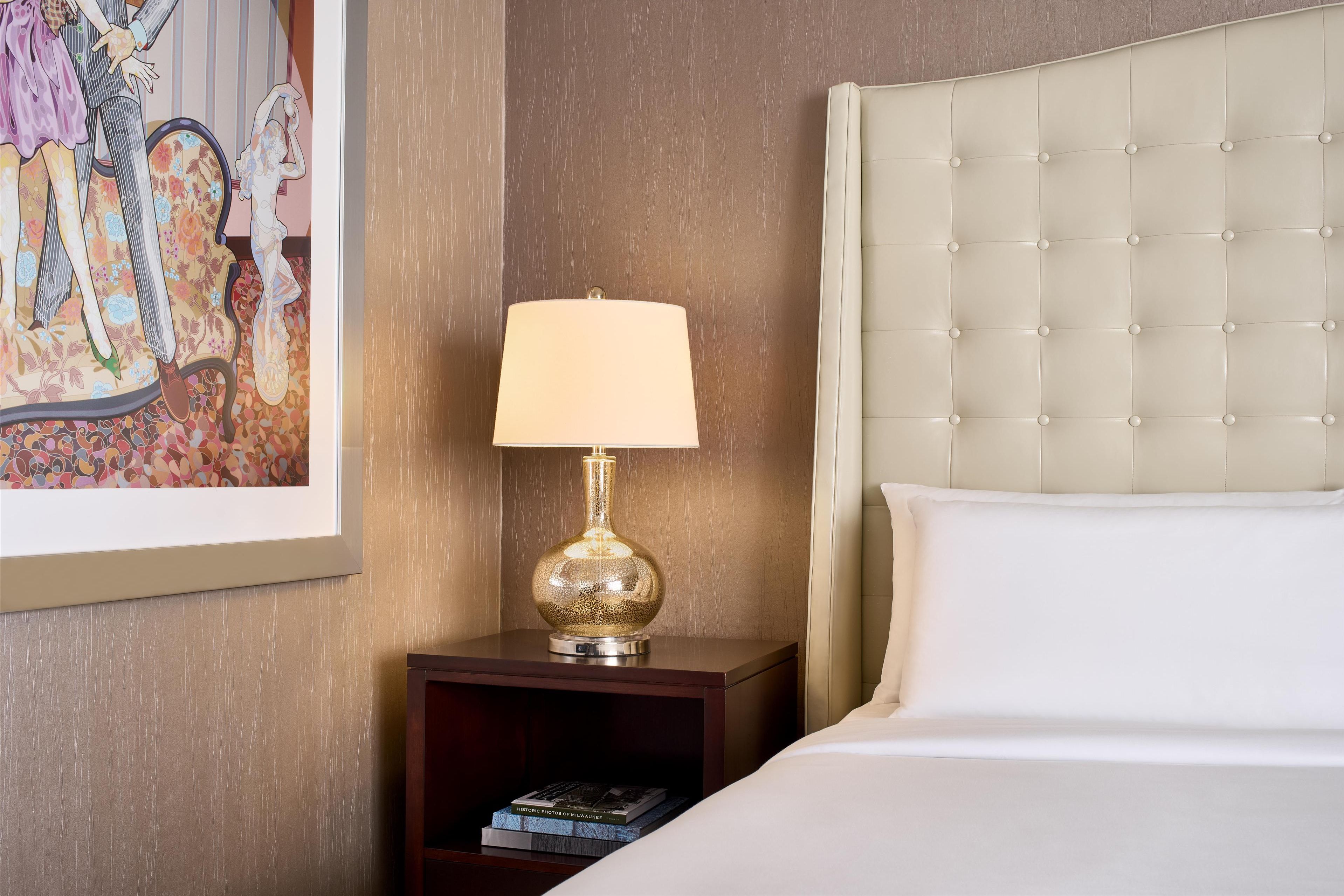 A neatly made bed with a tufted headboard, a bedside lamp, and a framed artwork on the wall.