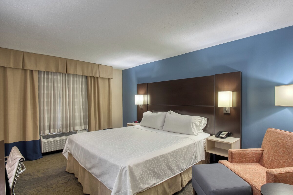 A hotel room with a bed, bedside tables, a chair, and a desk.