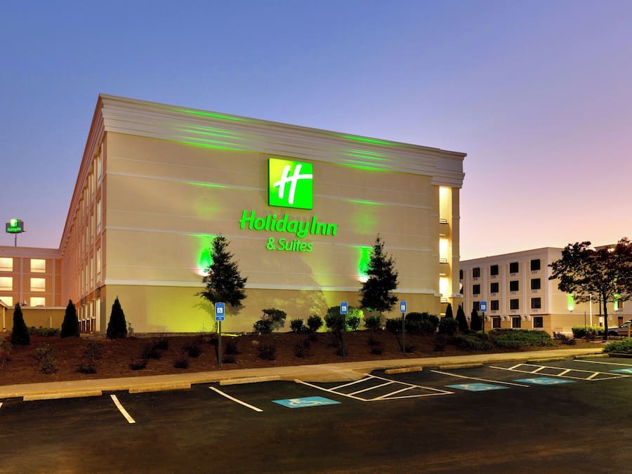 Um hotel Holiday Inn & Suites com uma grande placa, estacionamento e edifícios ao redor.