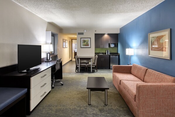 A hotel room with a TV, desk, chair, sofa, and kitchenette. - Holiday Inn Hotel & Suites Atlanta Airport-North by IHG (Atlanta)